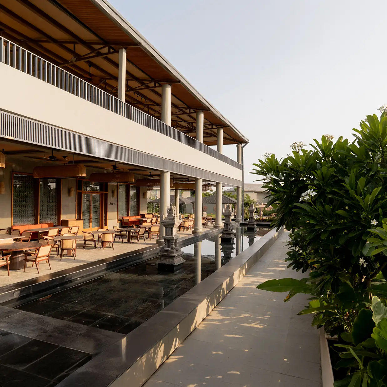A long dining terrace beside a reflecting pool in late light