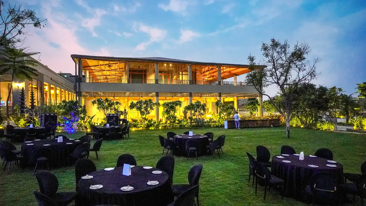 An open lawn set for an evening gathering before a lit pavilion